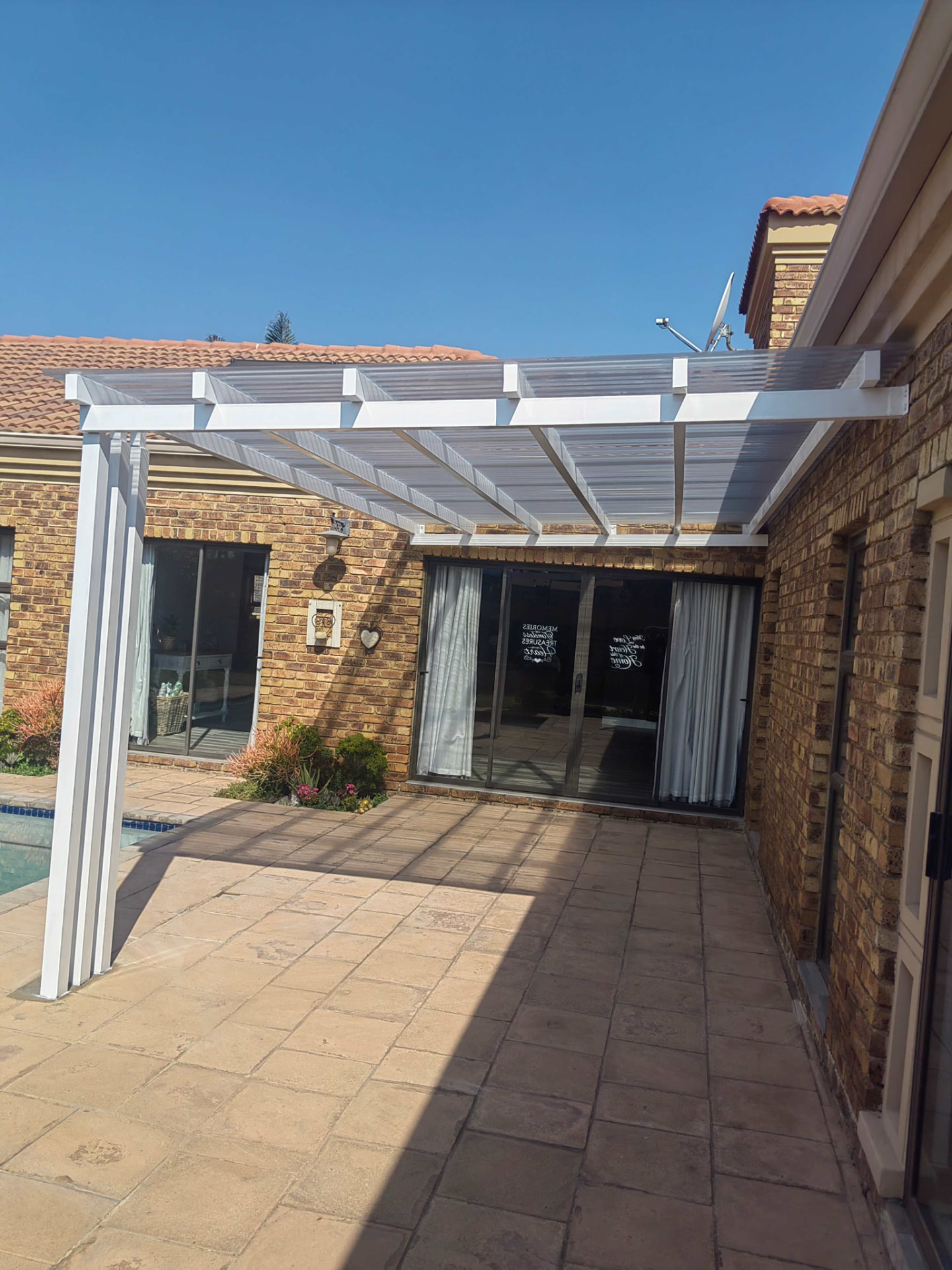 Pergola-style steel structure with clear polycarbonate roofing over a patio